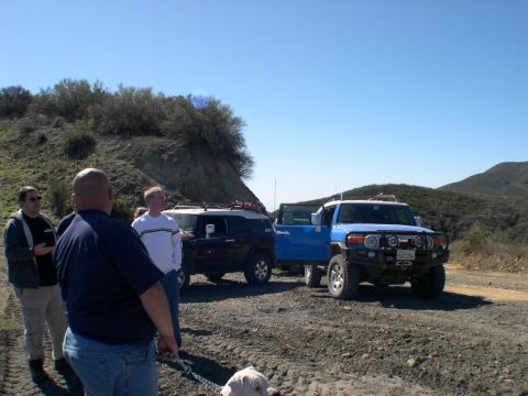 2007 Toyota FJ Cruiser - Two Toyota FJ Cruisers are parked on a dirt road with people and a dog nearby under a clear blue sky.