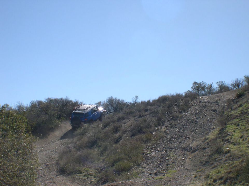 Blue 2007 Toyota FJ Cruiser climbing a steep dirt trail with brush on either side