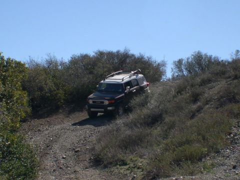 2007 Toyota FJ Cruiser - A dark 2007 Toyota FJ Cruiser navigates a dirt trail surrounded by dry brush.