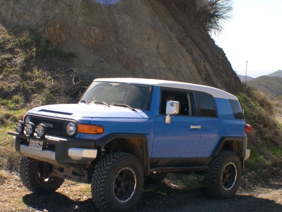 Blue 2007 Toyota FJ Cruiser parked on a dirt road with a rocky hillside behind it