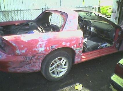 1991 Ford Bronco - This red sports car is undergoing repairs, with its doors open and bodywork showing signs of sanding and primer.