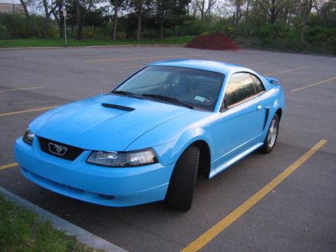 1991 Ford Bronco - A light blue Ford Mustang coupe (New Edge, ~1999-2004 SN95) shown from the front three-quarter angle, parked in an empty asphalt lot. The c…