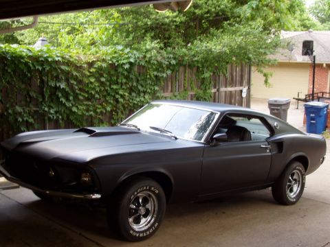 1991 Ford Bronco - A matte black 1969 Ford Mustang is parked in a driveway with a garage overhead.