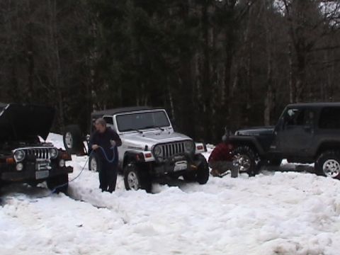 2005 Jeep Wrangler - Multiple Jeep Wranglers are stuck in the snow, with people attempting to use cables to free them.
