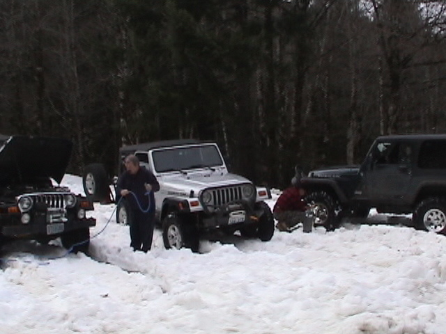 Three Jeep Wranglers in snow, one with hood open, people working with cables. 2005 Jeep Wrangler
