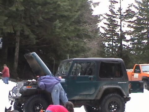 2005 Jeep Wrangler - A person works on the engine of a green Jeep Wrangler in a snowy environment, with another vehicle visible in the background.