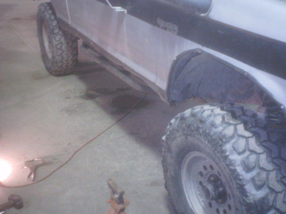 Passenger-side rocker of a silver Ford Ranger with tube rock slider and mud tires in a shop