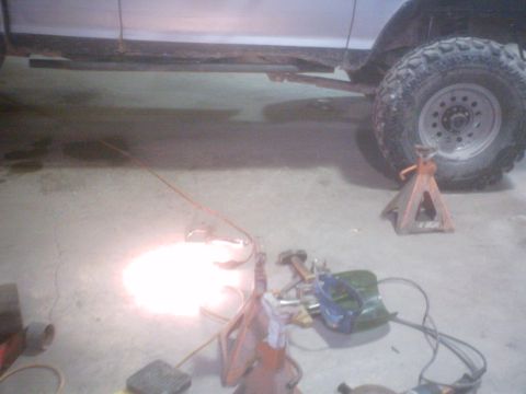 1990 Ford Ranger - A silver truck's side and wheel are visible, supported by jack stands, with welding equipment on the floor.