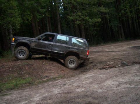 1977 Ford F-150 - A dark-colored Ford Explorer navigates a muddy incline in a wooded area.