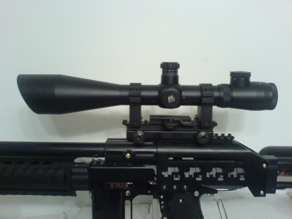 Black rifle with a large black scope mounted on top. The rifle has intricate cutouts on its side