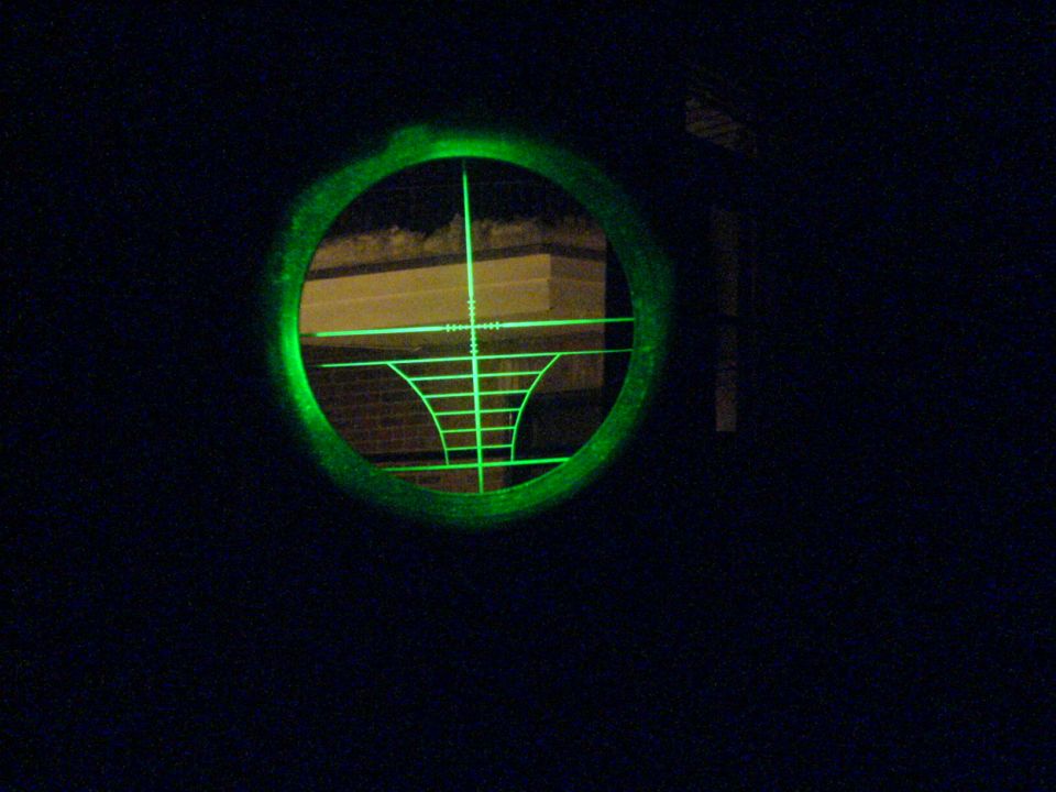 Green crosshairs in a scope view, looking at a brick building at night