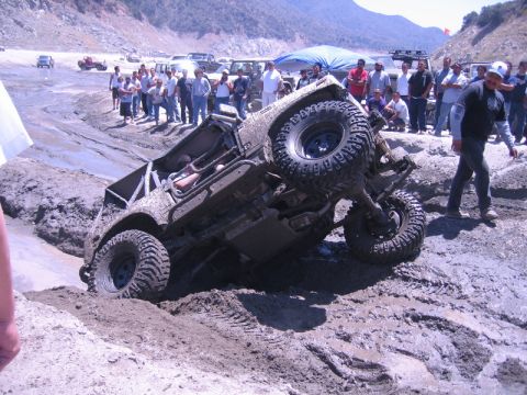1987 Suzuki Samurai - A group of spectators watches as an off-road vehicle struggles in a muddy terrain.