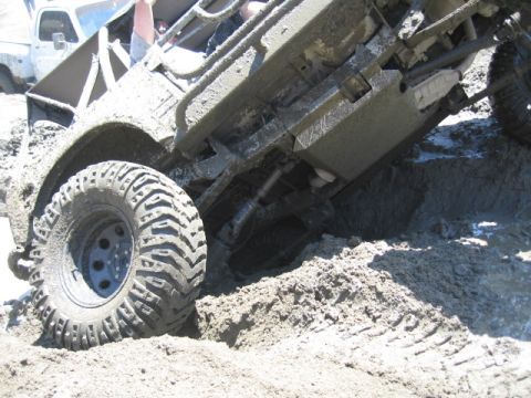 1987 Suzuki Samurai - An off-road vehicle is stuck deep in mud, with another vehicle partially visible in the background.