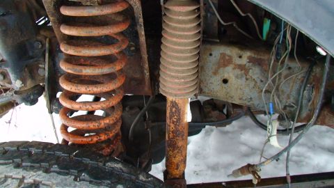 1979 Ford Bronco - Close-up view of corroded suspension parts, including a coil spring and shock absorber, on a vehicle.