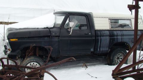 1979 Ford Bronco - This black pickup truck, likely from the late 1970s, is covered in snow and has a white camper shell on the bed.