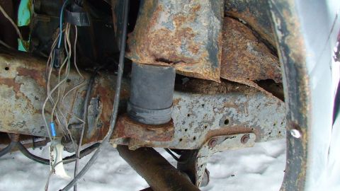 1979 Ford Bronco - Close-up view of heavily rusted vehicle frame and suspension components, with visible wiring and a rubber bump stop.