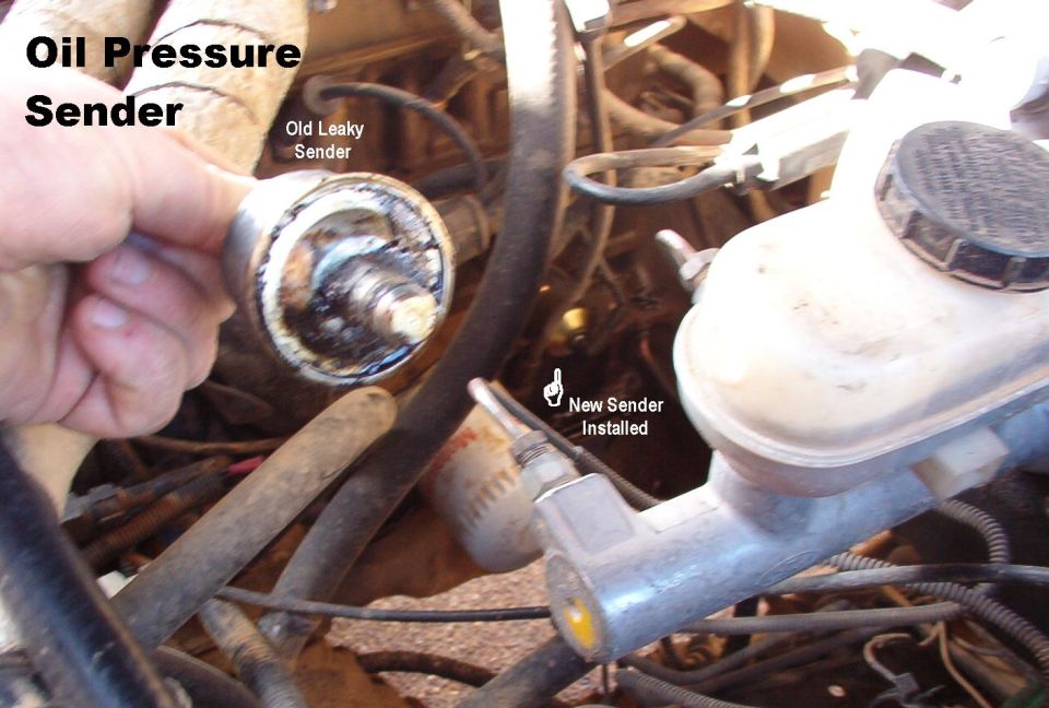 Hand holding old oil pressure sender next to engine with new sender installed