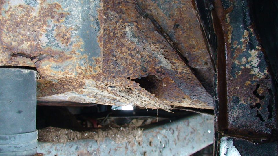 Severely rusted frame section with visible corrosion and damage. Part of a vehicle's undercarriage