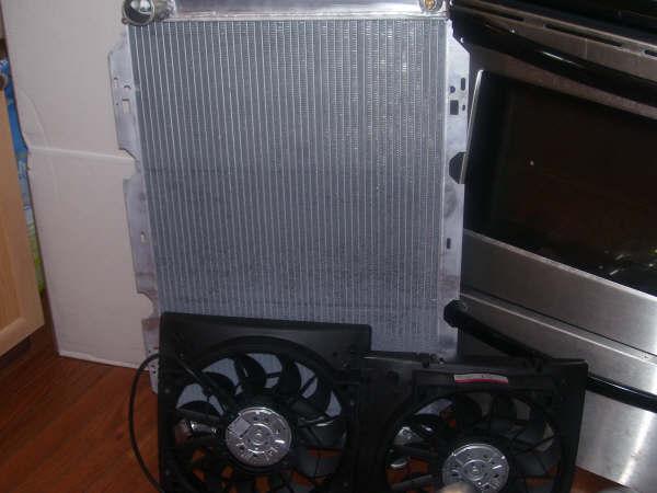 Aluminum radiator and black dual electric fan assembly standing in a kitchen next to a stove