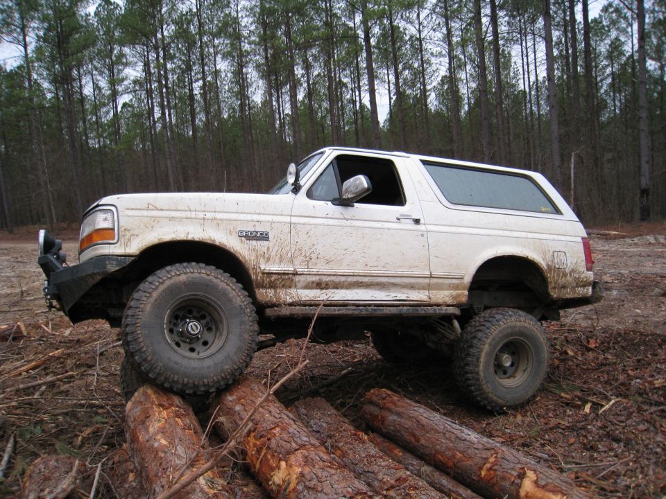 White 1996 Ford Bronco driving over logs in a wooded area