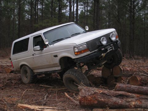 1996 Ford Bronco - A white Ford Bronco navigates a challenging off-road course with large logs.