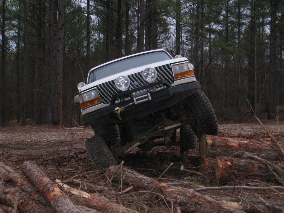 White 1996 Ford Bronco off-roading over logs