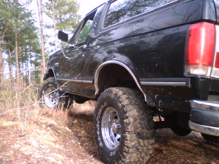 1990 Ford Bronco - A black Ford Bronco is seen from the rear quarter angle on an off-road trail.