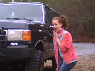1990 Ford Bronco - A woman stands next to a black SUV with large off-road tires. The vehicle's year is not identifiable from the image.