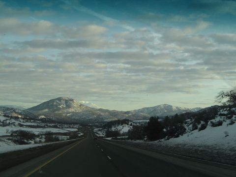 1989 Ford Bronco - Driving on a highway through a vast, snow-covered mountain range with scattered clouds.