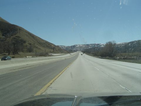 1989 Ford Bronco - A view from the driver's seat on a highway, with hills and distant mountains under a clear blue sky.