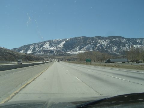 1989 Ford Bronco - A highway stretches towards distant, snow-dusted mountains under a clear blue sky.