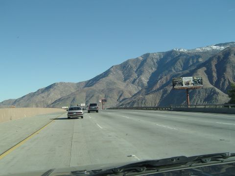 1989 Ford Bronco - A highway scene unfolds with vehicles traveling under a clear blue sky, with a billboard visible against a backdrop of mountains.