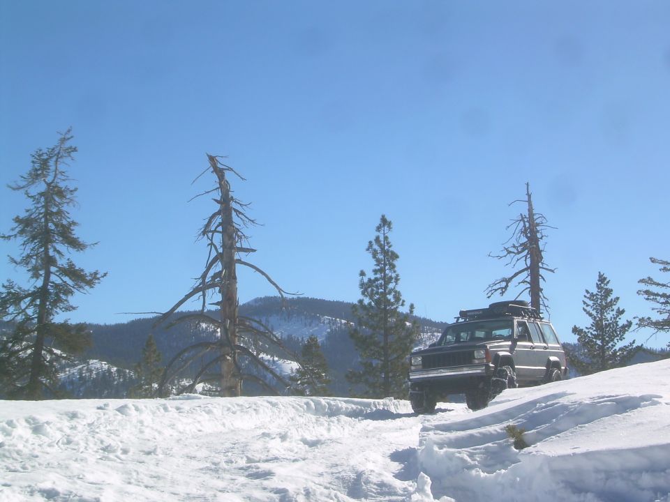 Dark SUV with roof rack on snowy road, likely a Jeep Cherokee XJ