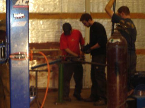 1992 Ford Bronco - Workshop scene with men operating a pipe bending machine and a large gas cylinder.