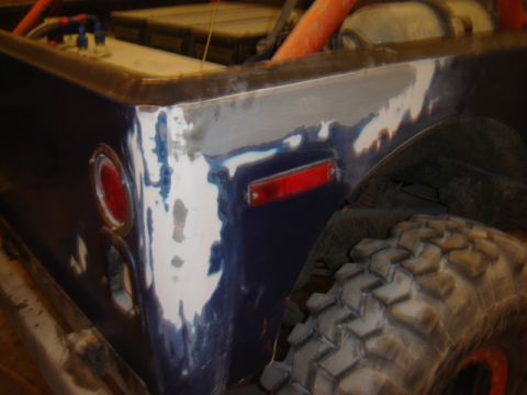 1992 Ford Bronco - This vehicle's rear fender is being prepped for paint, revealing primer and body filler around the taillight and wheel well-worn tire.