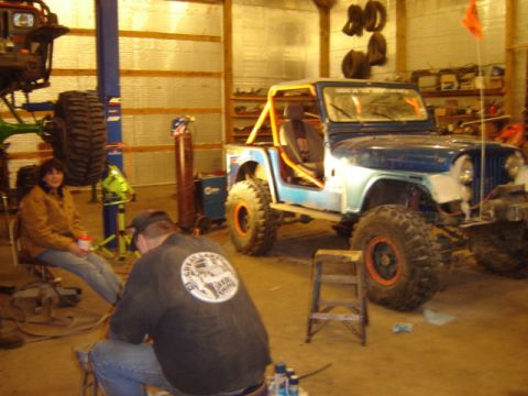 1992 Ford Bronco - Modified Jeep CJ-5 in a garage with another vehicle on a lift and two people present.