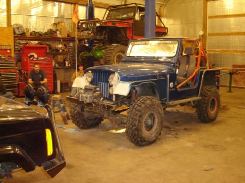 1992 Ford Bronco - A blue Jeep CJ is parked in a garage, with another vehicle on a lift in the background.