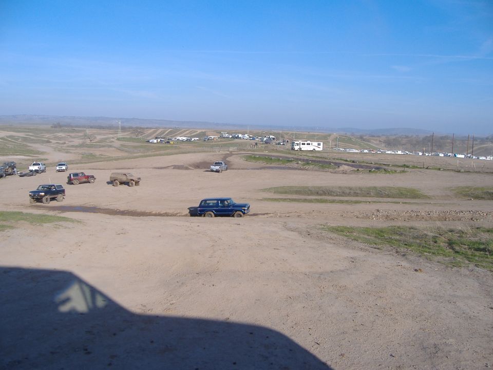 Several trucks and SUVs driving on a dirt track with spectators and RVs in the background