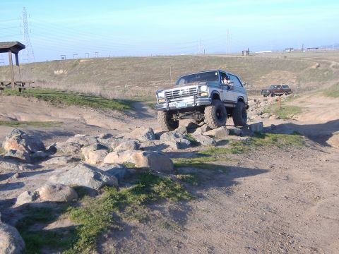 1986 Ford Bronco - This SUV is navigating a rocky off-road course under a clear blue sky.