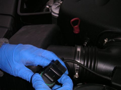 2002 BMW M3 - Close-up of a person replacing a mass air flow sensor in a vehicle's engine bay.