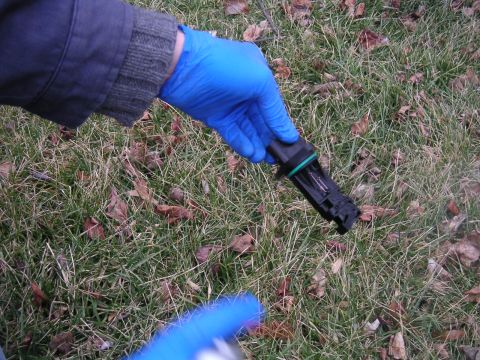 2002 BMW M3 - A mass air flow sensor is held in a gloved hand outdoors, with grass and fallen leaves in the background.