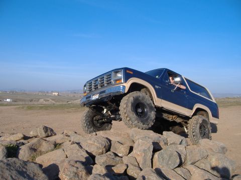 1986 Ford Bronco - Ford Bronco navigates a rocky obstacle course under a clear blue sky.