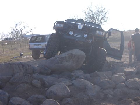 1986 Ford Bronco - A modified 1986 Ford Bronco navigates a rocky obstacle course with its driver door ajar.
