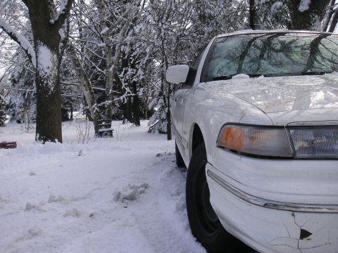 1997 Ford Crown Victoria - A white sedan sits parked in a snow-covered landscape, with trees and snow all around.