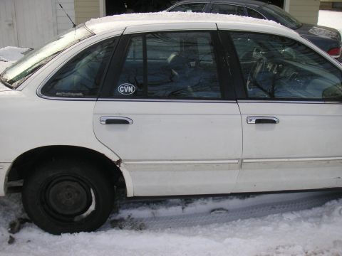 1997 Ford Crown Victoria - A white 1997 Ford Crown Victoria sedan is parked in the snow, with a 'CVN' sticker visible on the rear door window.