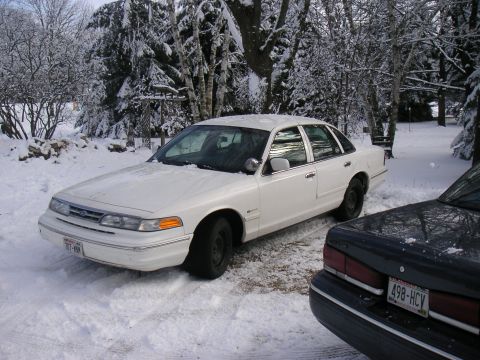 1997 Ford Crown Victoria - A white 1997 Ford Crown Victoria sits in a snowy driveway with trees in the background.