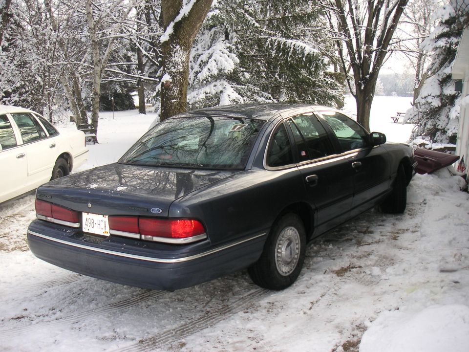 Dark blue sedan's rear quarter in snow. License plate 498-HCY. Another white sedan is partially visible to the left