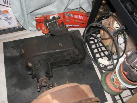 1984 Ford Bronco II - A transfer case sits on a mat next to a car jack and other automotive parts.