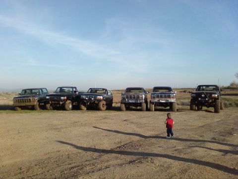 1995 Ford Bronco - A group of modified Ford trucks and SUVs are lined up in a dusty outdoor area.