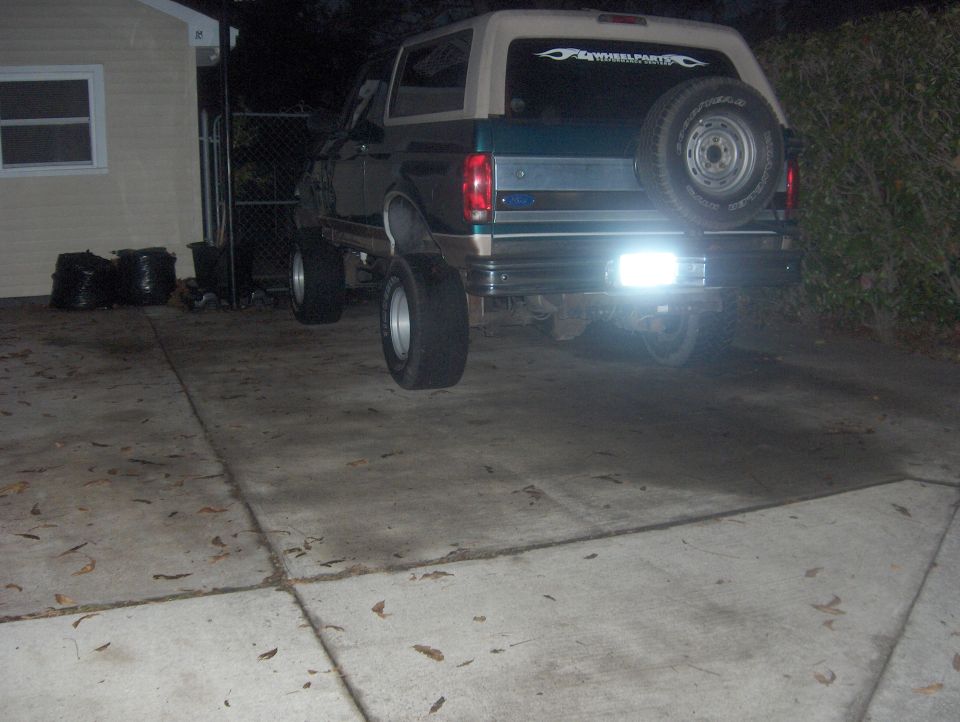 Rear of lifted green and tan Ford Bronco at night with spare tire and 4 Wheel Parts window decal